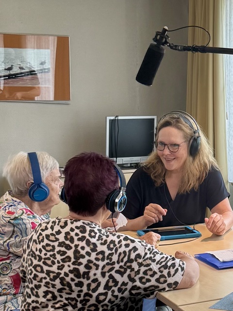 Seniorinnen und Frauke Hohberger unterhalten sich mit Kopfhörern und Mikrofon.